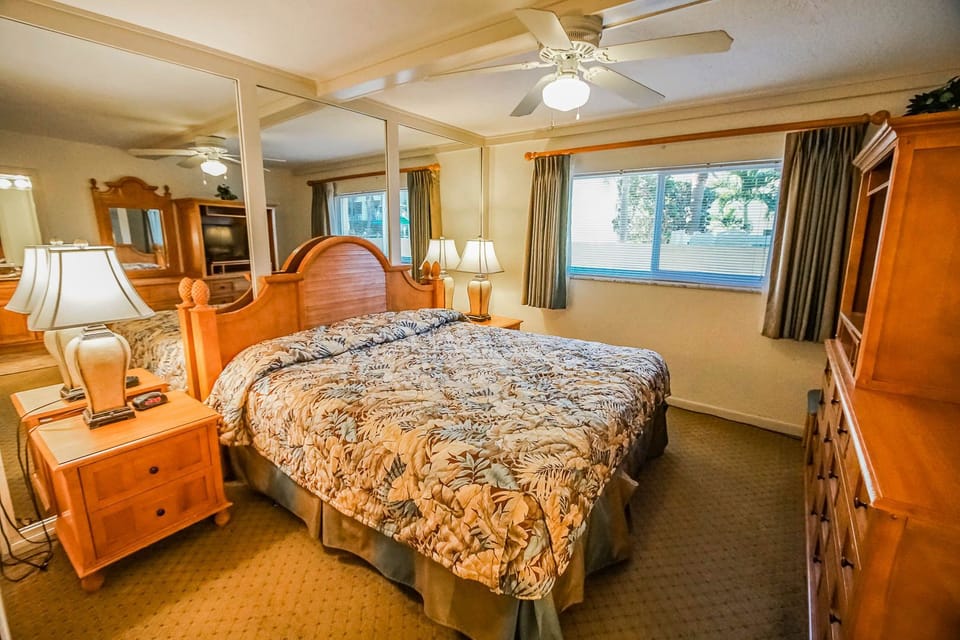 Relax in the king bedroom suite adorned with a cozy floral comforter and equipped with mirrored furnishings, offering both comfort and elegance for a restful night.