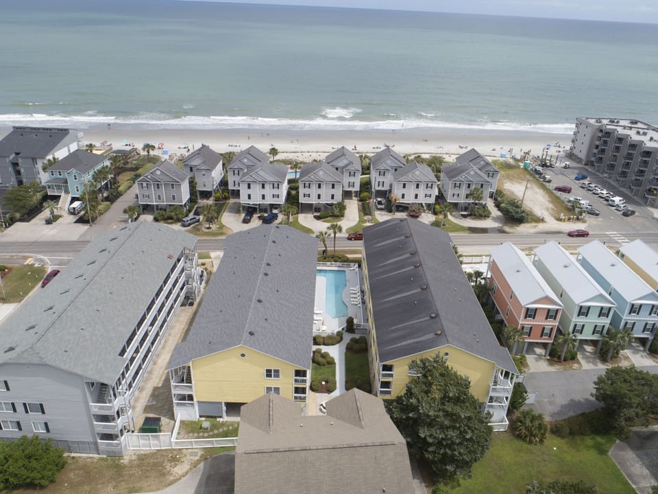This aerial view of Sandy Shores III highlights its prime beachfront location, outdoor pool, and easy access to nearby attractions in picturesque Murrells Inlet, SC.