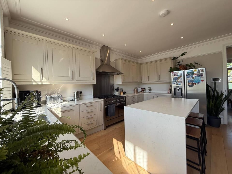 Bright and spacious kitchen featuring cream cabinetry, a sleek stainless steel range, and a large central island with bar seating. Sunlight pours in, highlighting the light wood flooring and modern appliances, creating a warm and functional cooking.