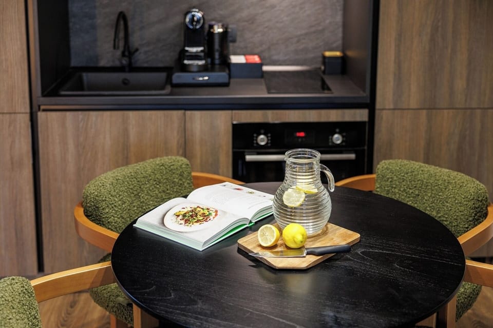 Stylish round dining table paired with textured green chairs and a fully equipped kitchenette, featuring an espresso machine, oven, and everything needed for a great meal.