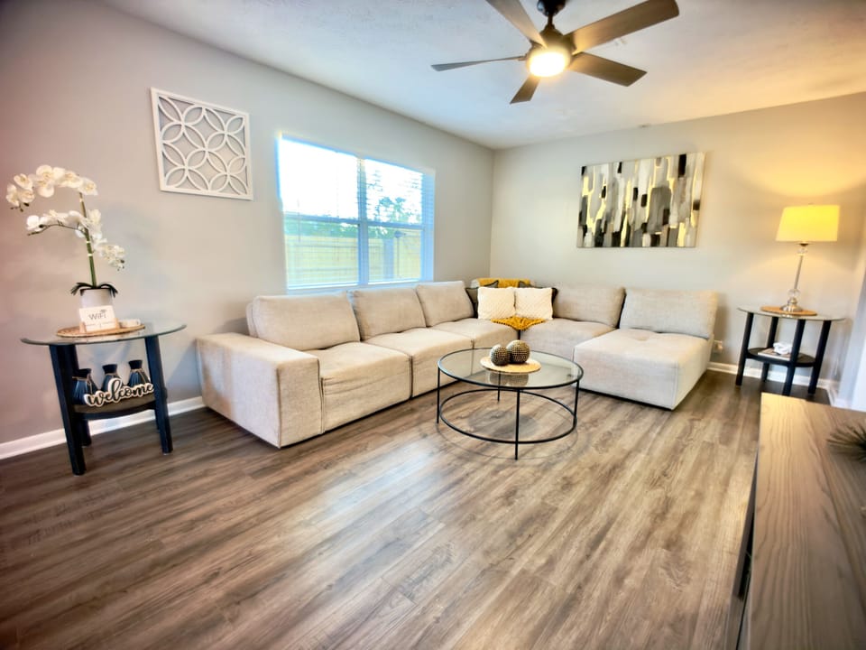 ☀️ Sun-filled and serene! This airy living room is flooded with natural light and features a plush sectional sofa, elegant décor, and hardwood floors — your home away from home! 🏡💛