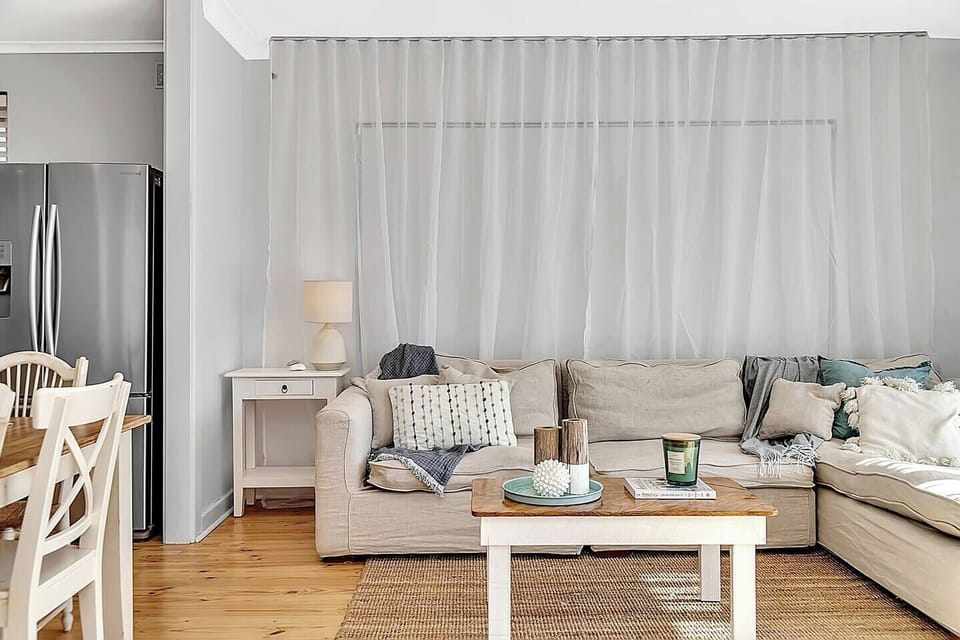 Unwind in the open-plan living area featuring an L-shaped sofa, soft throws, and relaxed textures—perfect for movie nights or breezy afternoon naps.