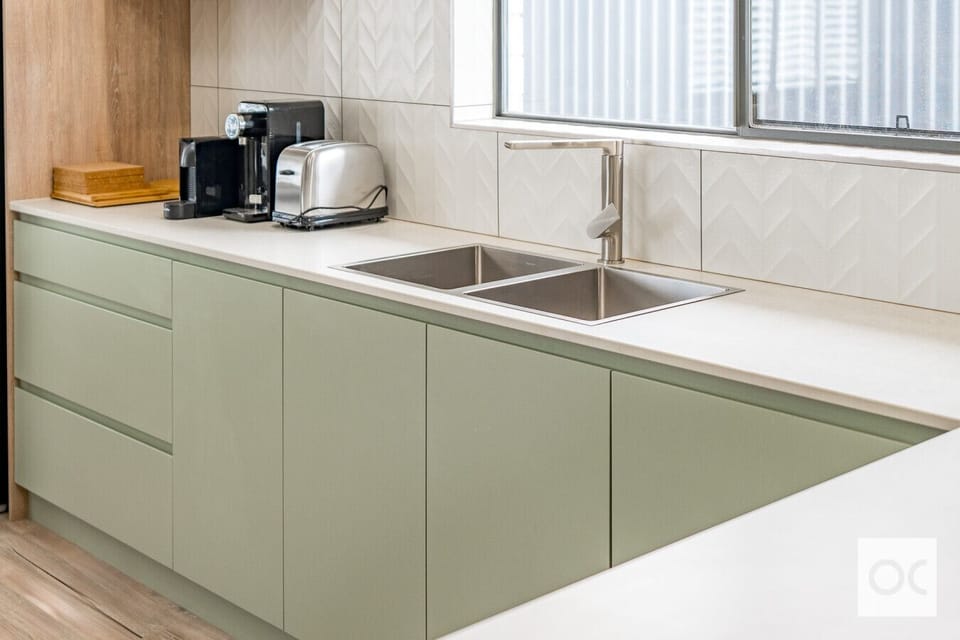 A stylish kitchen countertop with a modern sink and faucet. The cabinets below are painted in a light green color, and on the countertop, there are kitchen appliances such as a coffee maker and a toaster. The backsplash features a decorative chevron patte