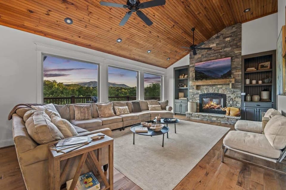 Spacious living room with panoramic mountain views, a cozy stone fireplace, and plenty of plush seating to unwind.