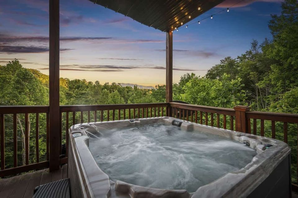 Unwind in the bubbling hot tub with mountain views and string lights, surrounded by peaceful forest vibes.