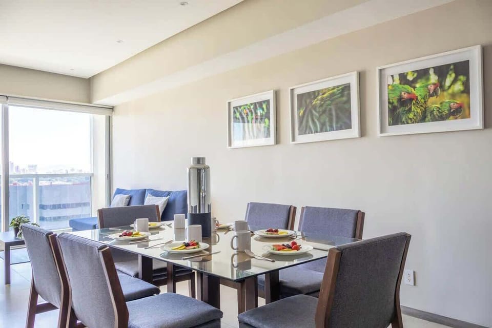 Bright dining area w/ table for shared meals, set beside large windows overlooking the skyline