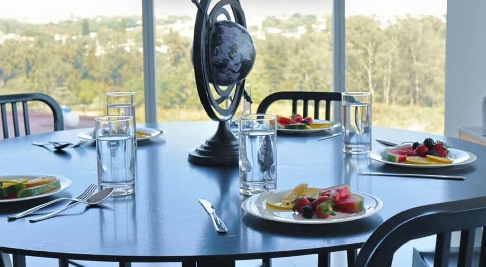 Round dining table set for a meal beside expansive city-view windows