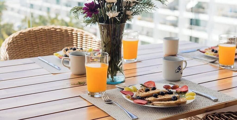 Sunny balcony table set w/ fresh drinks & flowers for a relaxed start to the day