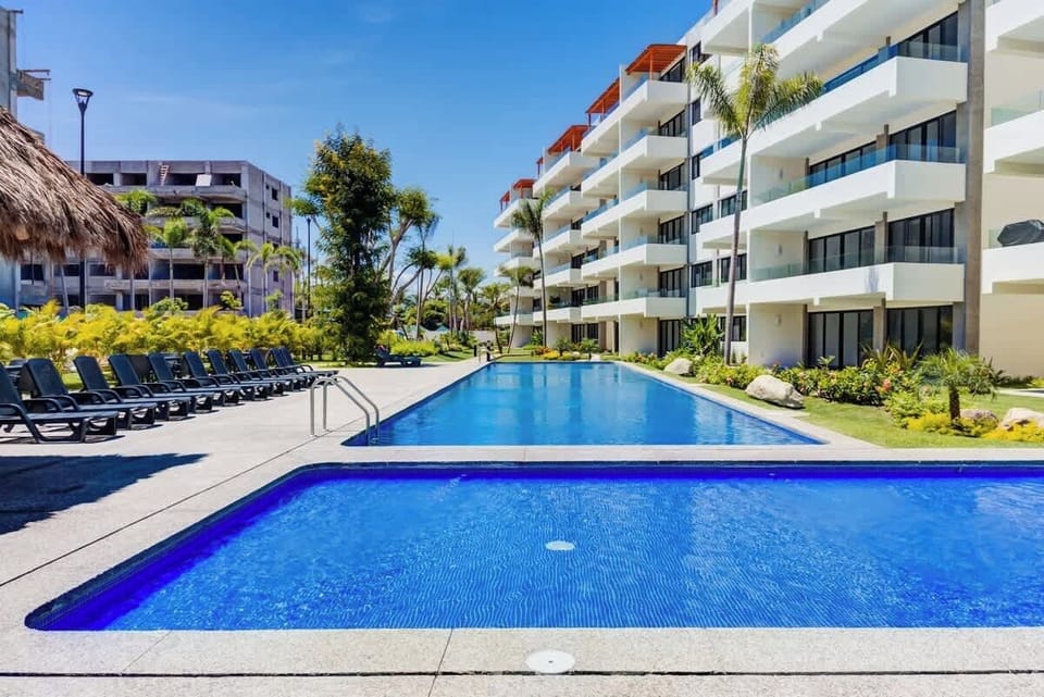 Shared pool surrounded by lounge chairs and lush landscaping in a bright courtyard setting