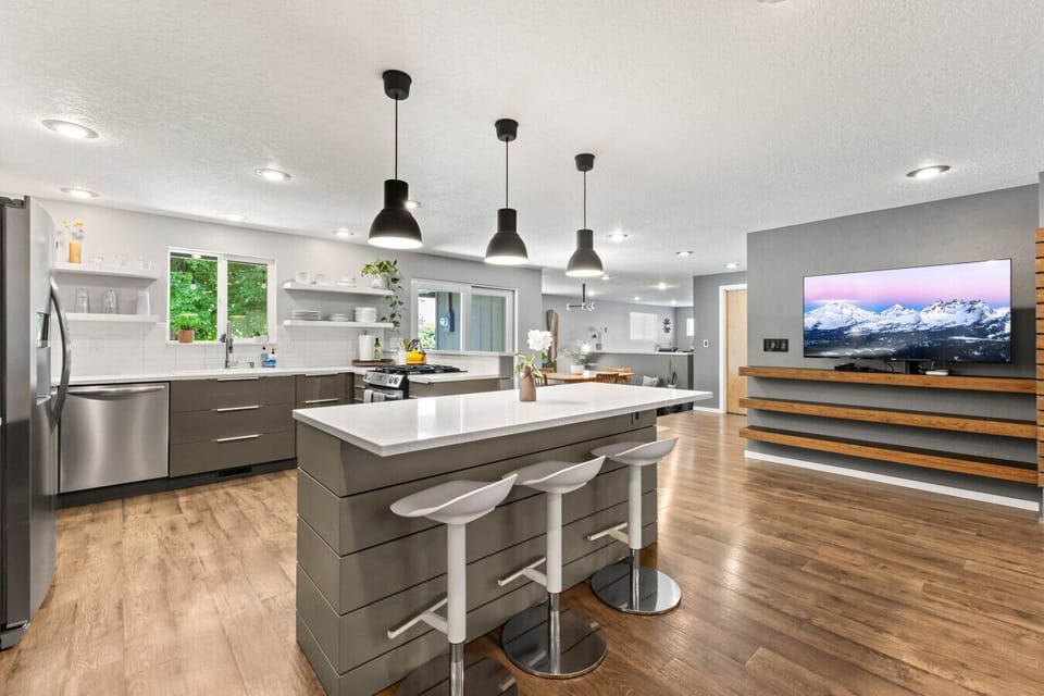 Kitchen with a large island, bar seating for 4, and a TV in the living room just behind.
