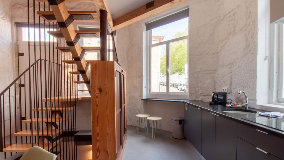 A kitchen that blends tradition and modernity, with stone walls, large windows, and a sculptural staircase centerpiece. #RusticModern #DesignKitchen #NaturalMaterials
