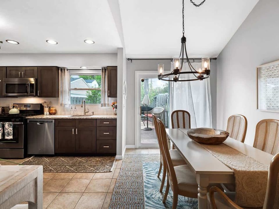 Elegant dining space with seating for six ️, set beneath a statement chandelier . Natural light flows in through sheer curtains, creating a bright and welcoming area for meals, games, or conversation .