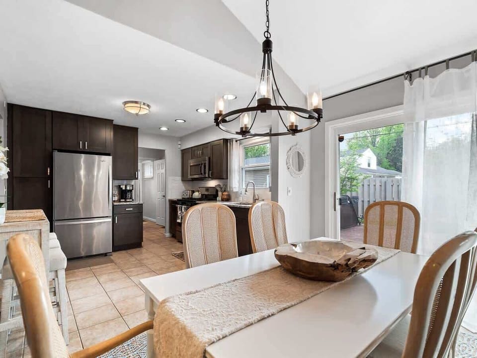Elegant dining space with seating for six ️, set beneath a statement chandelier . Natural light flows in through sheer curtains, creating a bright and welcoming area for meals, games, or conversation .