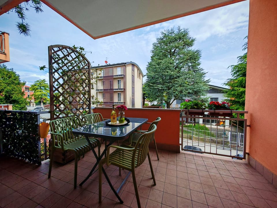 Large balcony furnished with table and chairs, ideal for outdoor breakfasts or relaxing with a glass of wine. The outdoor space, surrounded by plants and flowers, offers a pleasant view of the quiet residential neighborhood of Peschiera del Garda.