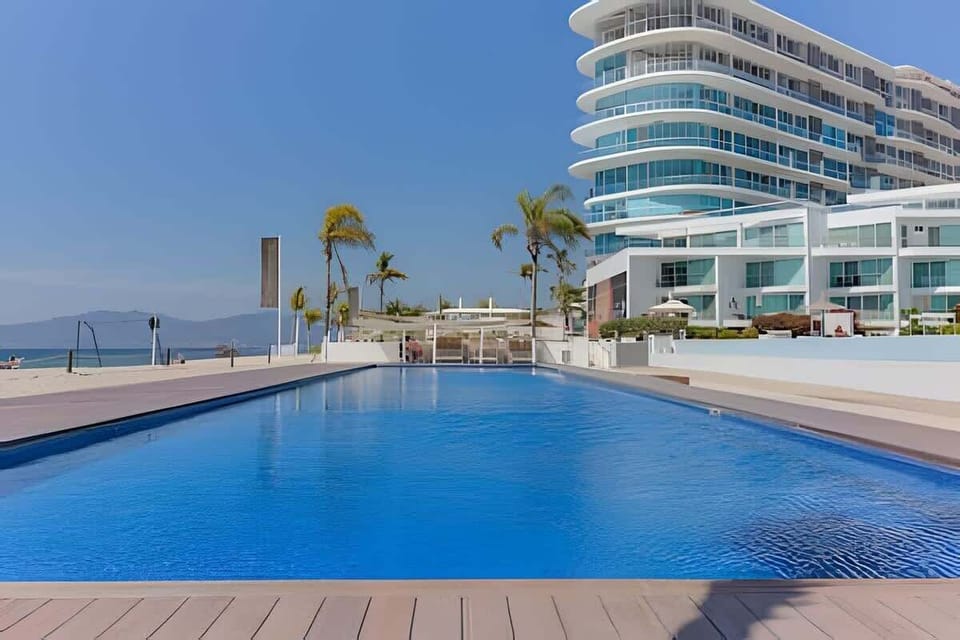 Large shared resort pool framed by the curved modern building & sunny deck space