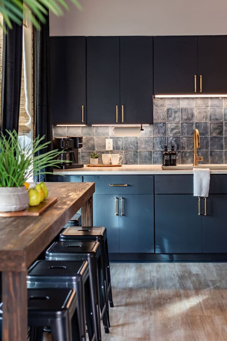 A dramatic dark kitchen with teal tile backsplash and brass accents.