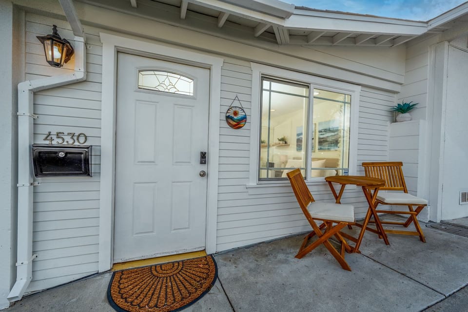 A beautiful front patio with a bistro-style seating area, perfect for enjoying your morning coffee or evening wine. The white exterior, warm lighting, and inviting atmosphere create the perfect getaway.