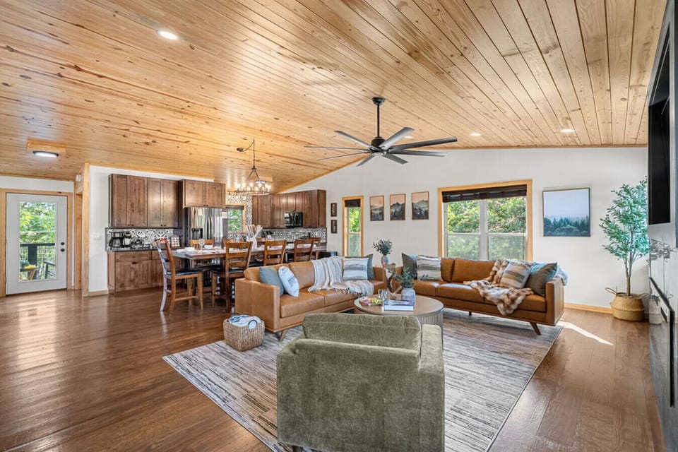 The living room on the Main Level is light and bright with large windows, a 65` Samsung Smart TV, modern linear electric fireplace, and a vintage-style record player—perfect for relaxing with a glass of wine, charcuterie, and a good Dolly record.