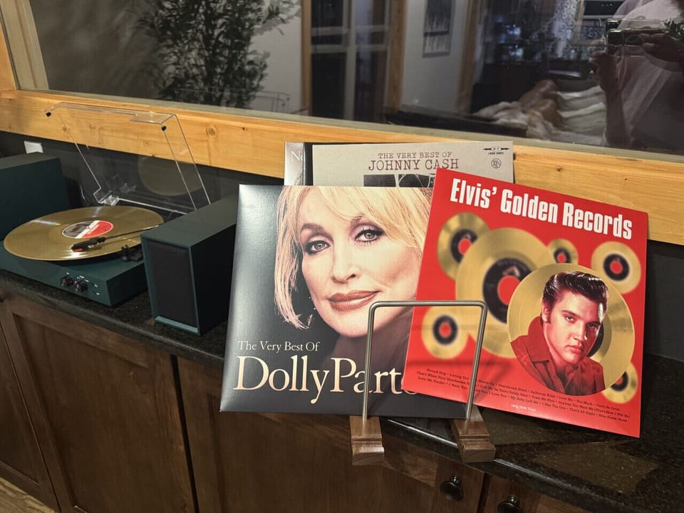 The living room on the Main Level is light and bright with large windows, a 65` Samsung Smart TV, modern linear electric fireplace, and a vintage-style record player—perfect for relaxing with a glass of wine, charcuterie, and a good Dolly record.