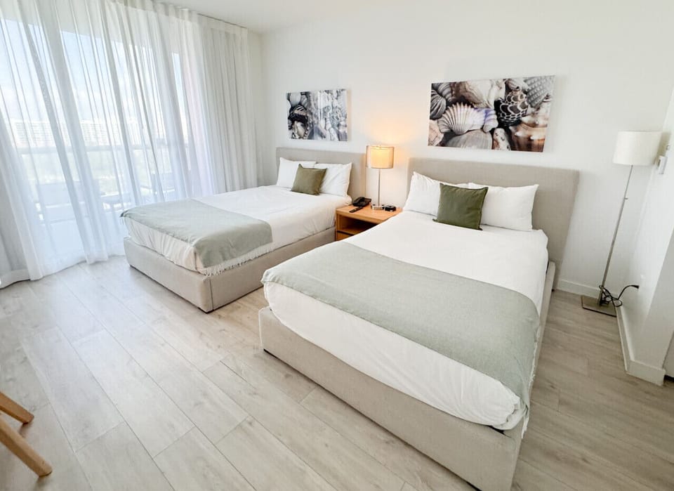 Spacious bedroom with a two beds, flat-screen TV, and bright natural lighting.