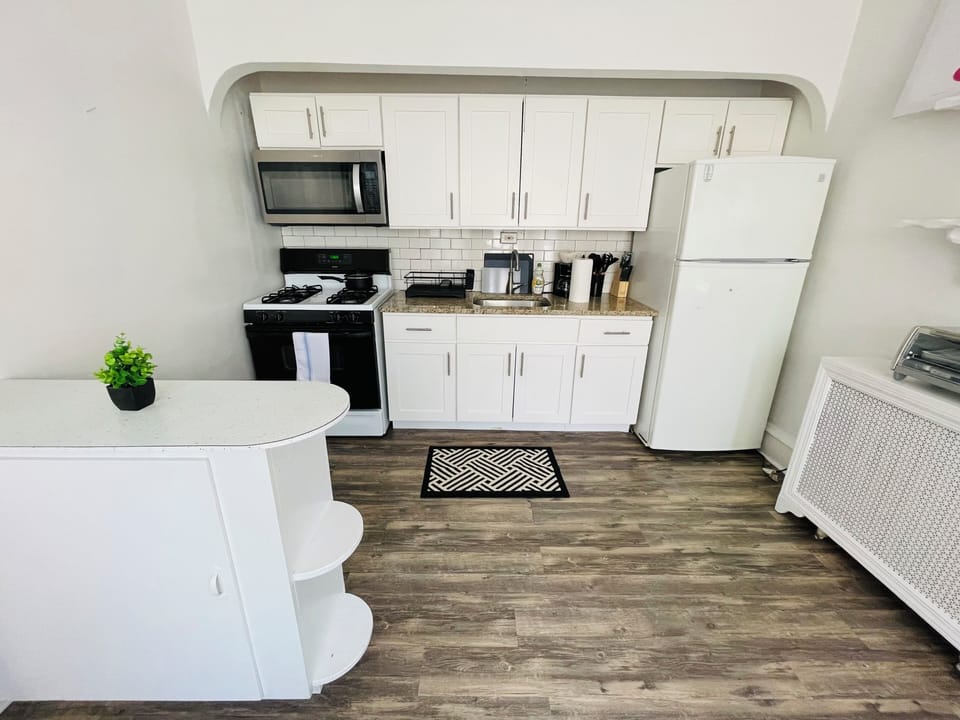Bright and updated kitchen featuring white cabinets, modern backsplash, full-size fridge, microwave, and gas stove. Includes open shelving, ample counter space, and contemporary flooring—ideal for everyday cooking and casual dining.