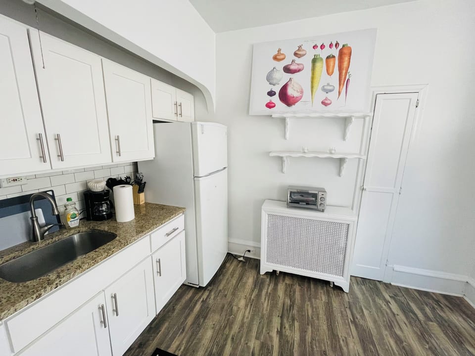 Bright and updated kitchen featuring white cabinets, modern backsplash, full-size fridge, microwave, and gas stove. Includes open shelving, ample counter space, and contemporary flooring—ideal for everyday cooking and casual dining.