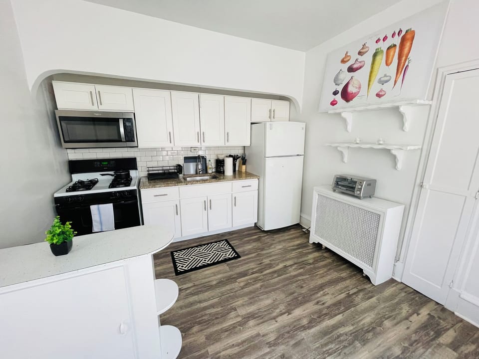 Bright and updated kitchen featuring white cabinets, modern backsplash, full-size fridge, microwave, and gas stove. Includes open shelving, ample counter space, and contemporary flooring—ideal for everyday cooking and casual dining.