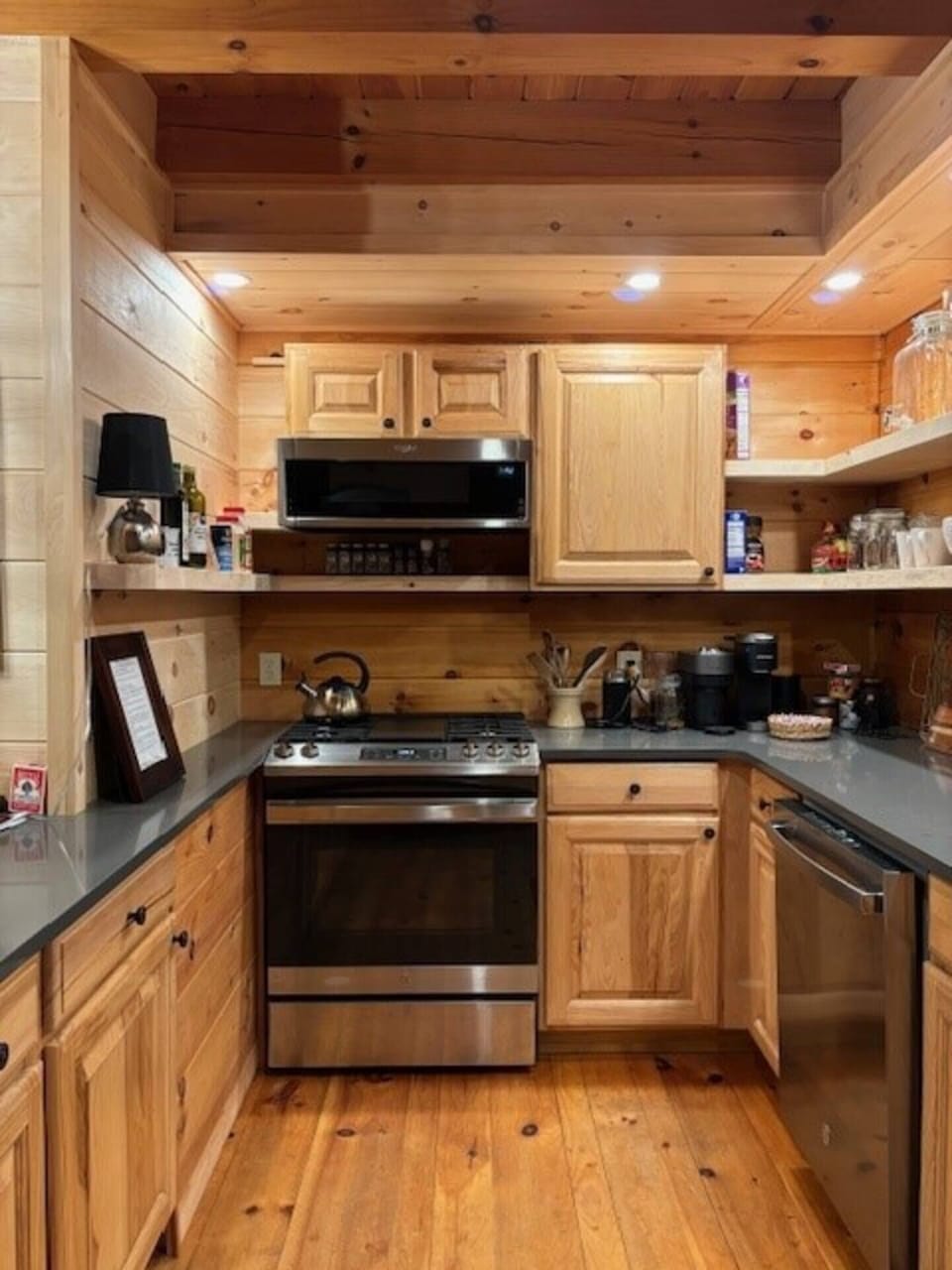Complete and well lit kitchen with solid wood open shelves and stainless steel appliances.