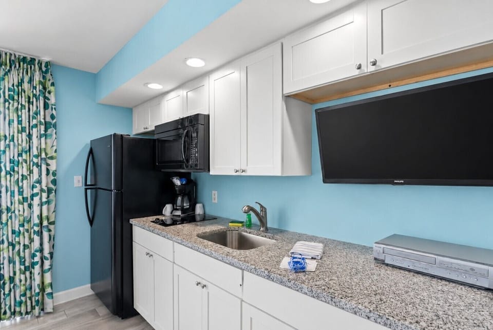 Coastal-style kitchen with full-size refrigerator, microwave, sink, two-burner cooktop, coffee maker, and Smart TV designed for easy beach living.