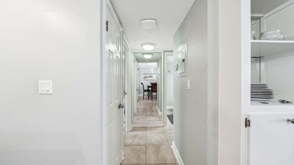 This clean, well-lit hallway with soft gray walls and built-in shelving leads to a coastal-style dining area.