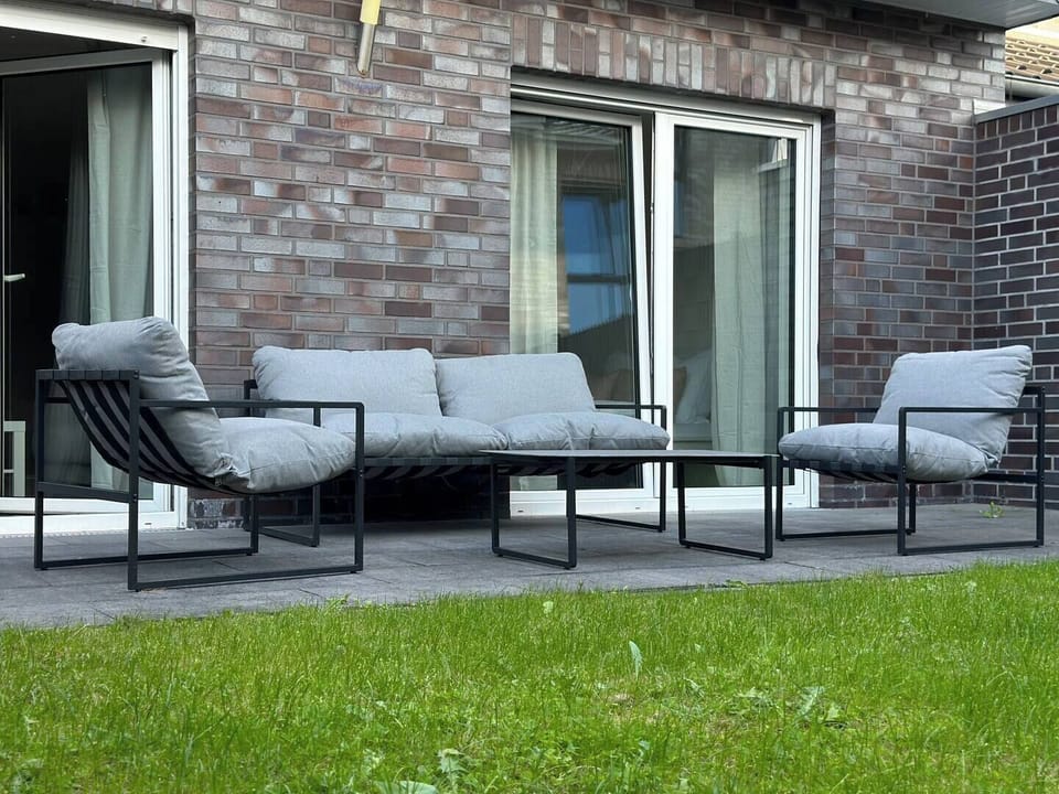 Terrasse mit moderner Lounge aus zwei Sesseln, Sofa und Beistelltisch – gemütliche Sitzecke am Garten für entspannte Stunden im Freien.