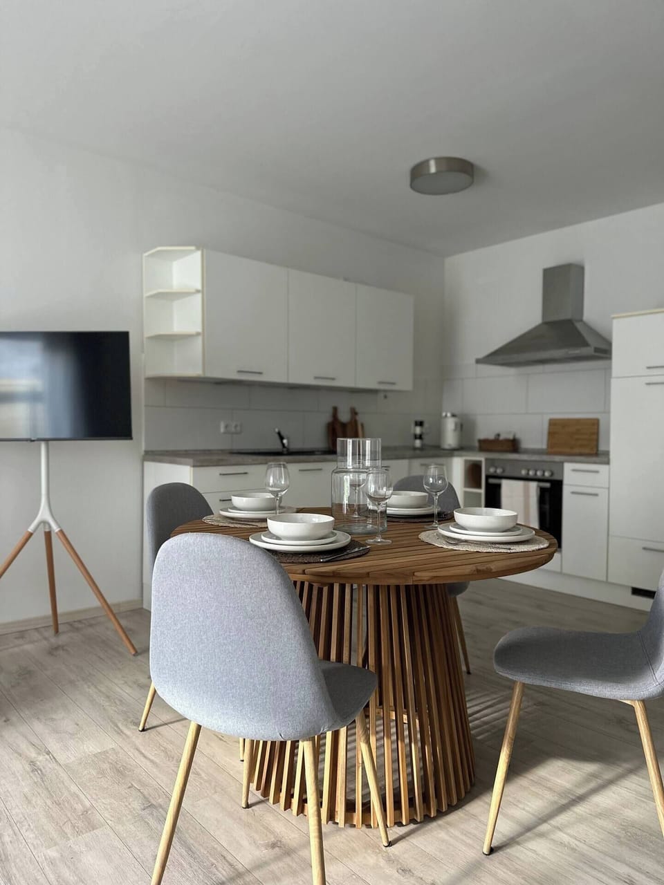 Offene Wohnküche mit rundem Holzesstisch, gedeckter Tafel und TV auf Stativ – modern, freundlich und ideal für gemeinsame Abende.