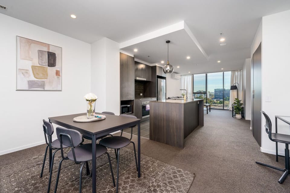 Modern and inviting social space featuring an open kitchen, a comfortable dining area, and a lounge with clear views of the pool and Woden city.