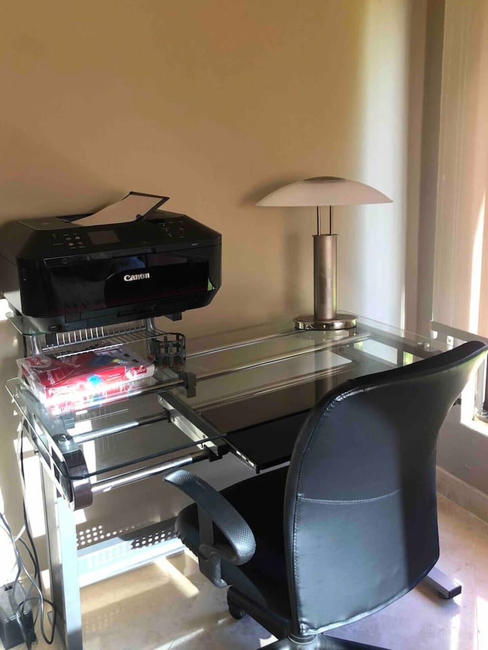 Dedicated workspace with a glass desk, an office chair, and a printer.