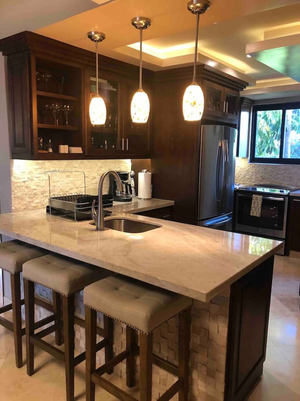 Kitchen with a quartz countertop island, three barstools, and a stainless steel refrigerator.