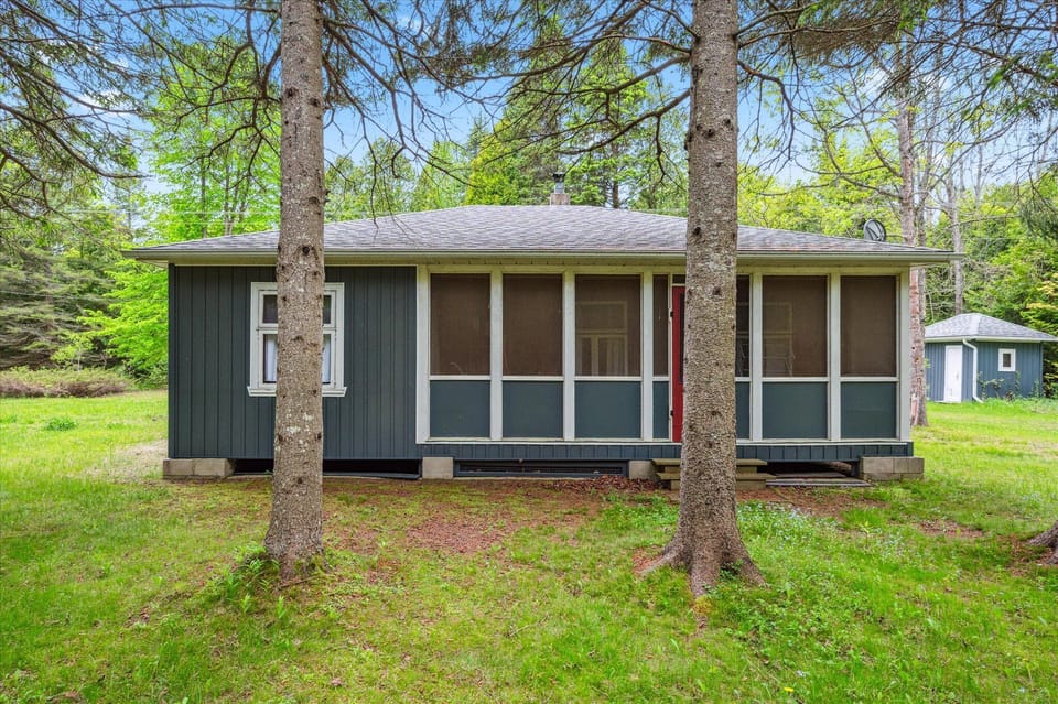 The screened-in front porch is a cozy retreat from bugs and sun. With a pop of red on the door and classic screened panels, it’s the ideal spot for morning coffee, afternoon reading, or evening chats under the trees.
