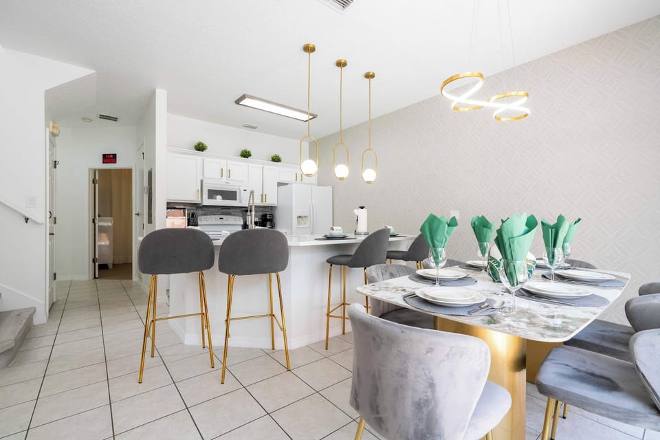Gather family and friends in this bright, all-white gourmet kitchen & dining area! Features a sleek island with four plush gray bar stools, a chic marble-top table with velvet chairs, gold accents, and pendant lighting for stylish meals.