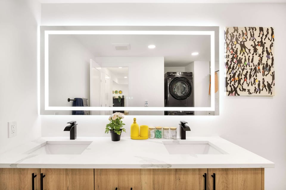 A sleek, spa-like bathroom featuring a dual-sink vanity with LED lighting, contemporary black fixtures, and warm wood cabinetry.