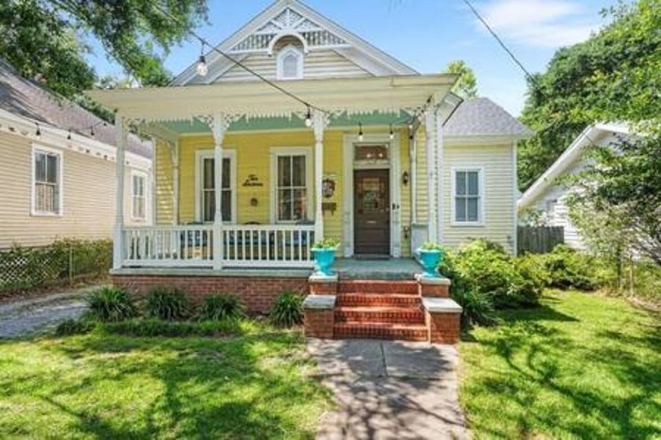 This charming historic cottage in Mobile complemented by a welcoming front porch that exudes classic Southern character. The architecture is defined by intricate white Victorian-style "gingerbread" scrollwork.