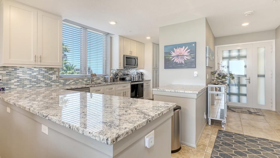 Granite countertops and glass tile backsplash highlight the U-shaped kitchen with stainless steel appliances and window view.