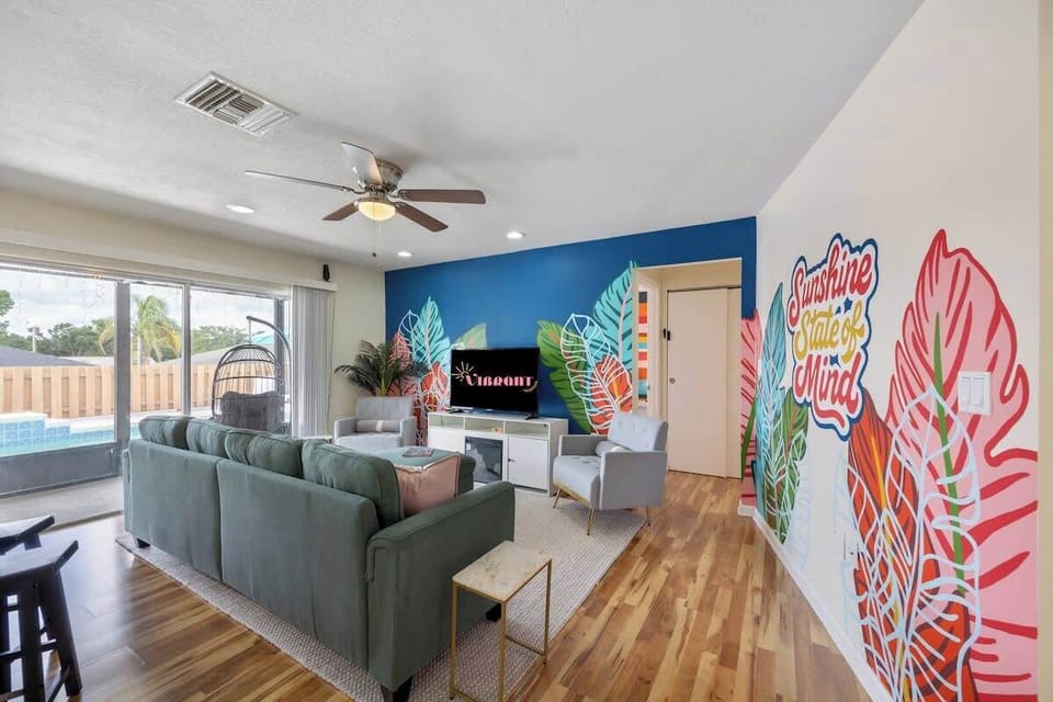 Feel instantly uplifted in this colorful, tropical-inspired living room—where bold murals, cozy seating, and pool views create the perfect fall getaway
.