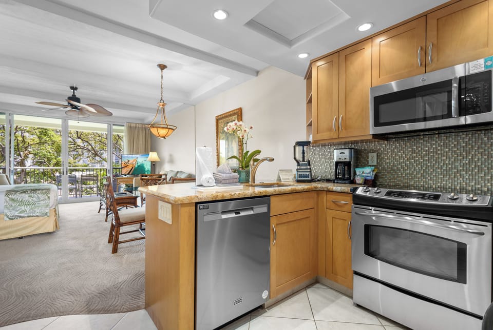 Your vacation kitchen awaits with stainless steel appliances, granite counters, and mosaic tile backsplash—open to a sunlit living space where island breezes flow through and your tropical getaway begins.