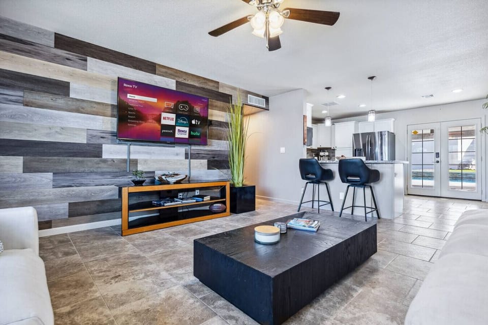 Open concept designed living area with a modern entertainment setup and a striking accent wall, flowing seamlessly into a well-appointed kitchen with convenient bar seating.