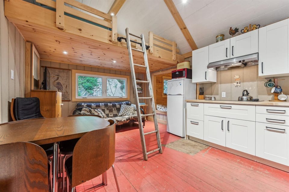 The open-concept layout brings together the kitchen, dining, and living areas under vaulted ceilings — with a loft ladder leading to treetop views and a cozy hideaway up top.