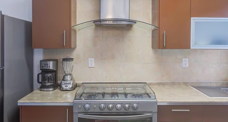 Modern kitchen stove & hood framed by warm cabinetry & tiled backsplash