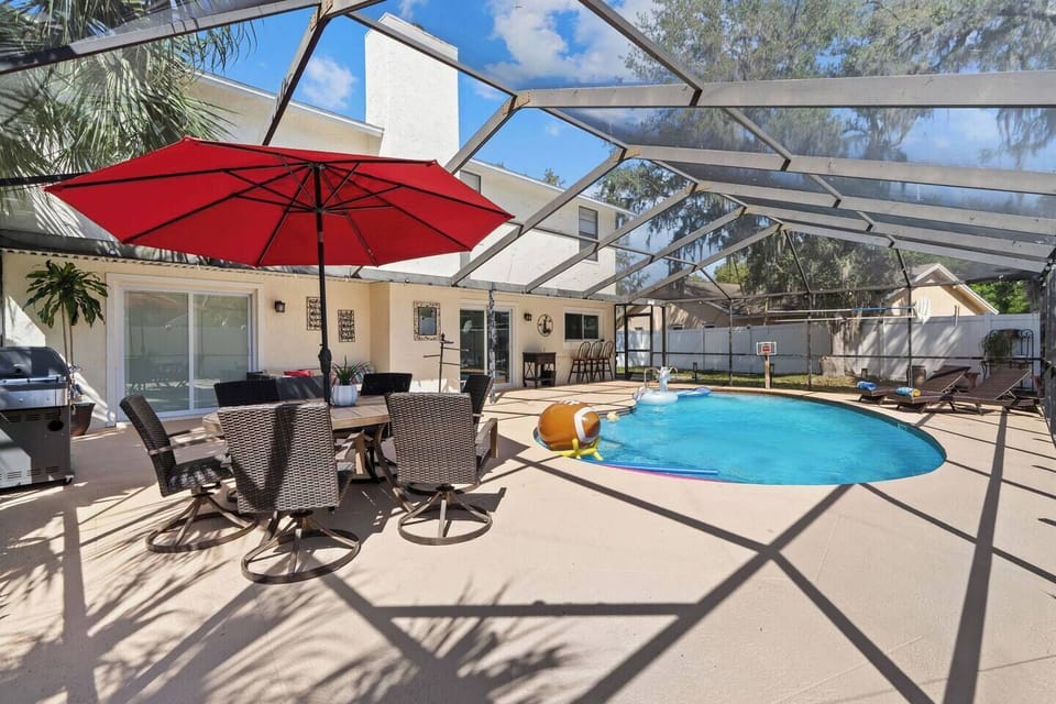 Step into your private oasis, a sparkling pool, comfy lounge seating under a bold red umbrella.