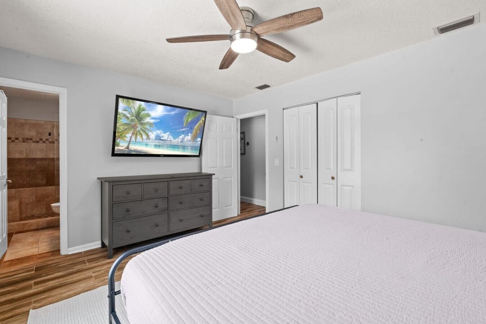 Primary suite features a king bed, en suite bathroom, Smart TV, and serene backyard and pool views.