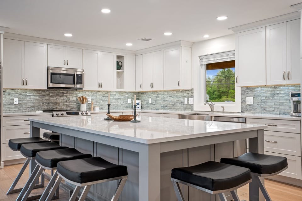 Modern kitchen with white cabinets, large island, appliances, and wooden floor.