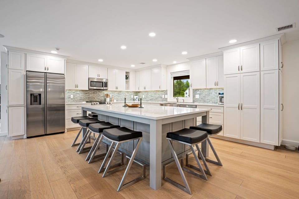 Modern kitchen with white cabinets, large island, appliances, and wooden floor.