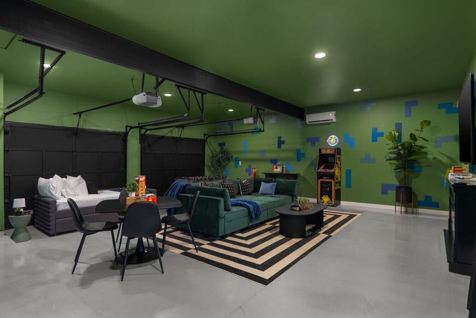 Fun-filled game and lounge room featuring arcade games, a cozy seating area, smart TV, dining space, and even a comfy bed—perfect for entertainment and relaxation all in one!
